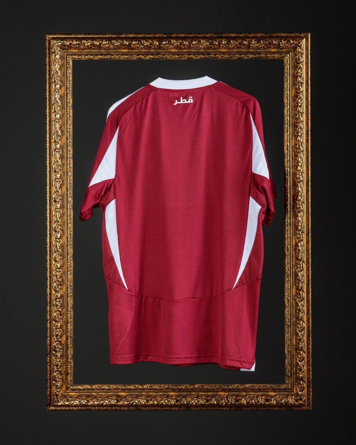 Back view of a red Qatar football jersey with white side panels, framed inside a gold ornate frame against a dark background.