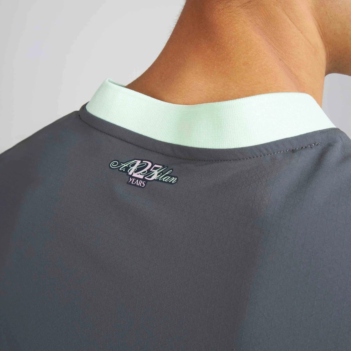Back of a dark gray shirt with a pale mint collar and a small embroidered logo near the neck.