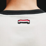 Close-up of the back of a white mesh shirt with a small red, white, and black badge reading 'UNITED' on the upper back.