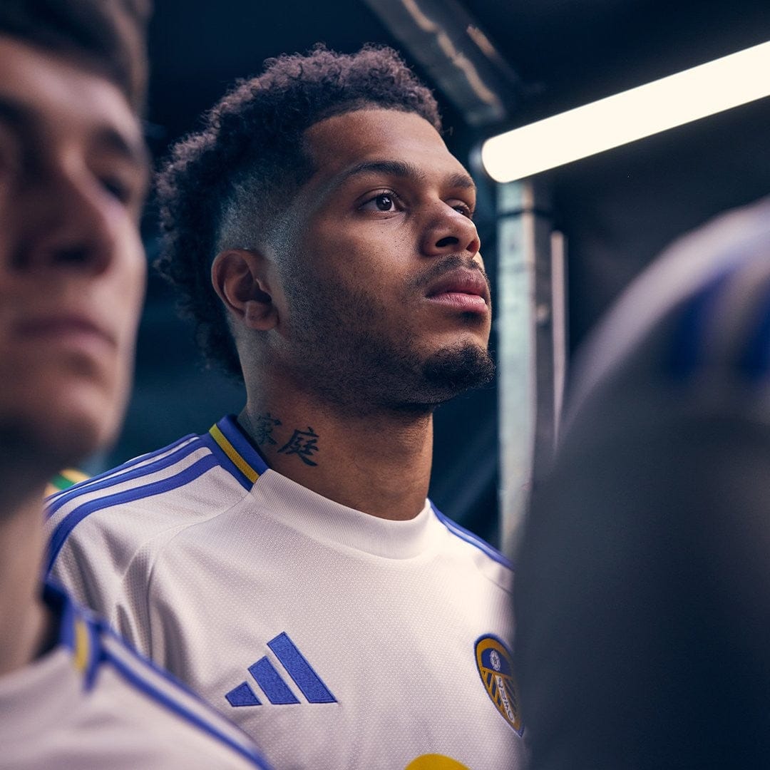 L4XxiD76Qa9canF | UAE SPORT STORE Soccer player in a white jersey with blue trim stands in a tunnel, looking ahead.