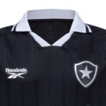 LJ | UAE SPORT STORE Dark navy soccer jersey with a white V-neck collar, featuring a Reebok logo on the left and a shield with a star on the right.