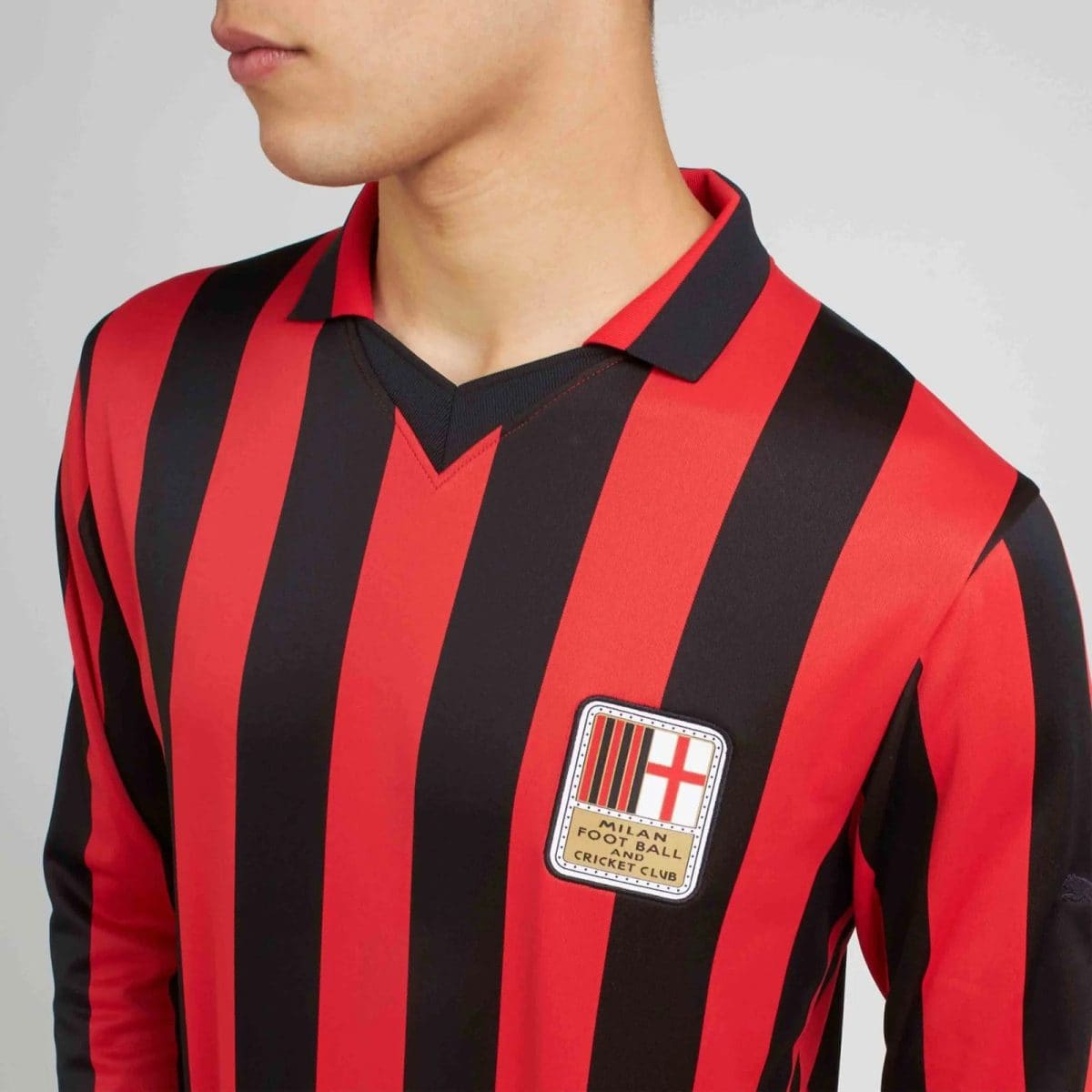 Close-up of a person wearing a red-and-black striped soccer jersey, with a shield-like chest patch visible on the left.