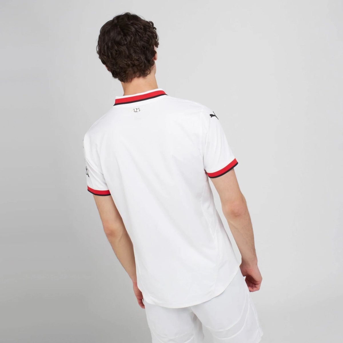 Back view of a person wearing a white polo shirt with red and black striped collar and sleeve cuffs.