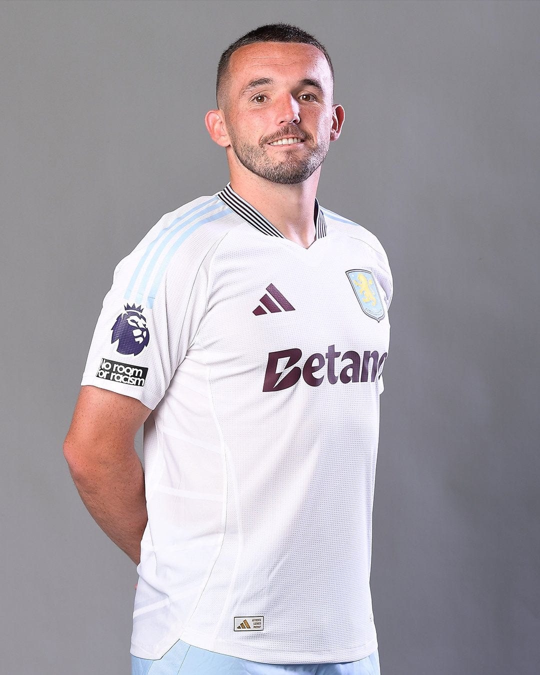 LsvIoLuoSyhHpwF | UAE SPORT STORE Professional footballer posing in a white Aston Villa jersey with Betano sponsor and Premier League badge.