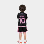 Back view of a child wearing a black football jersey with pink 'MESSI 10' and pink trim, standing with arms crossed.