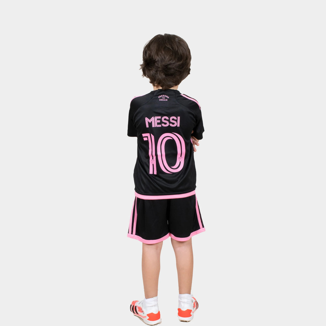 MIMIBlackBB-result_1280x_a2817e2e-16c6-4130-96b3-00a7d27fd0da Back view of a child wearing a black football jersey with pink 'MESSI 10' and pink trim, standing with arms crossed.
