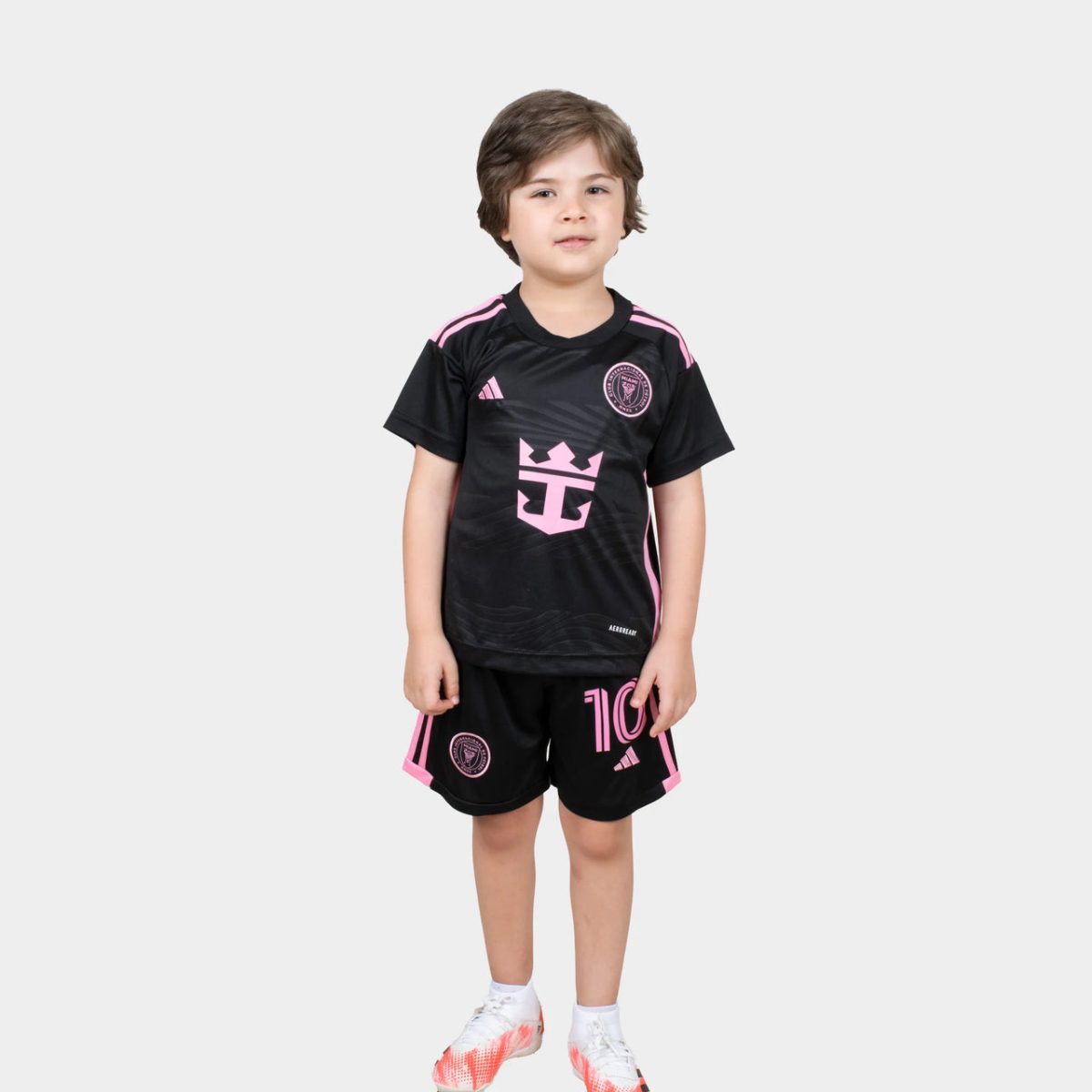 Young child wearing a black and pink soccer jersey and matching shorts, standing and facing the camera.