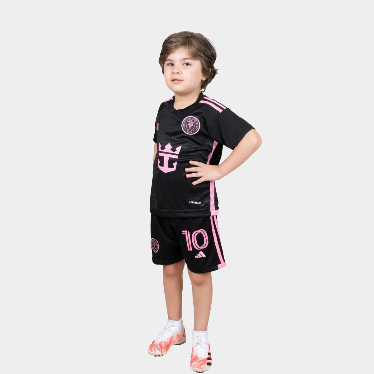 Young boy standing with hands on hips, wearing a black and pink soccer kit with the number 10 on his shorts.