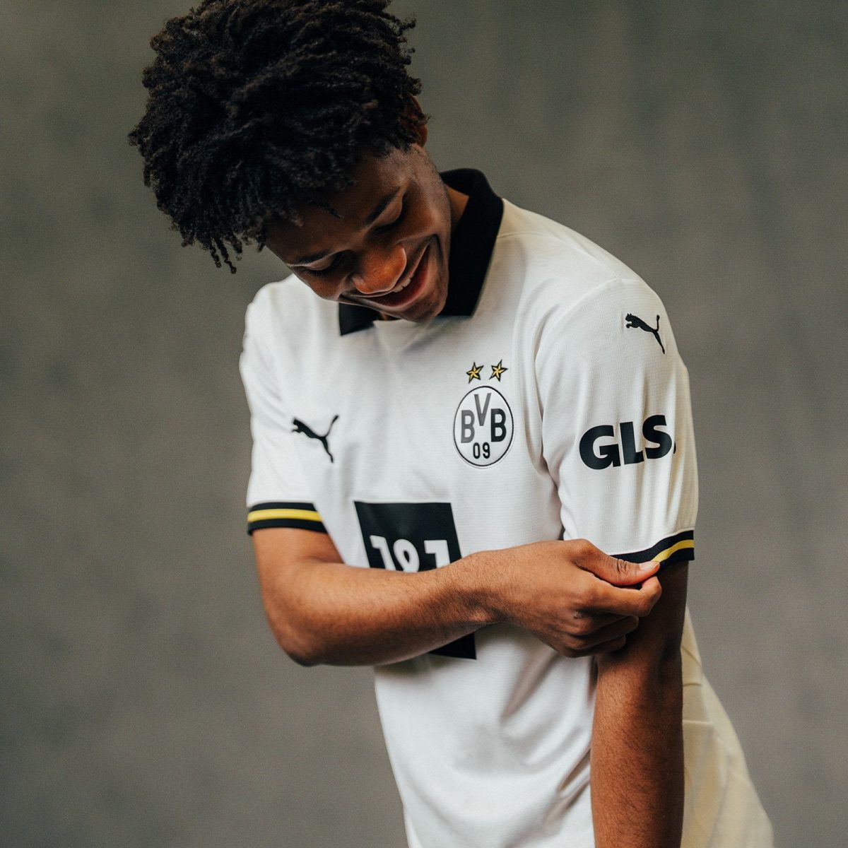 Young man wearing a Borussia Dortmund jersey smiles while adjusting his sleeve.