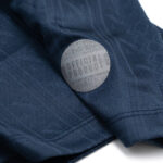 Close-up of navy fabric with a round silver badge that reads 'OFFICIAL PRODUCT'.
