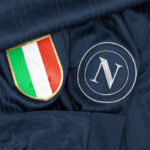 Close-up of a navy jersey showing an Italian flag shield and a silver circular 'N' logo.