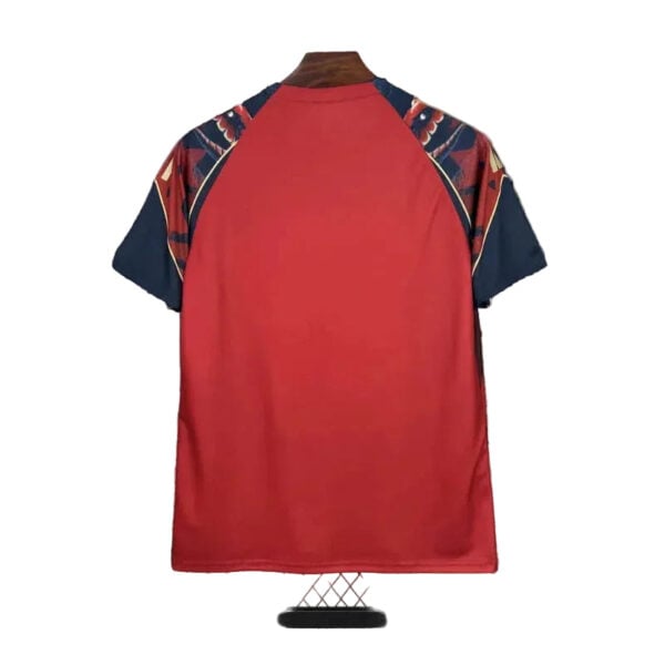 Back view of a red athletic jersey with navy sleeves and decorative shoulder panels, displayed on a stand.