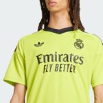 MbCQ4pVj3wmRYEu | UAE SPORT STORE Close-up of a person wearing a neon yellow Real Madrid jersey with the Emirates Fly Better sponsor and club crest on the chest.