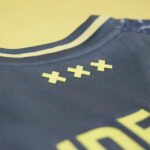 Close-up of a dark athletic jersey with three yellow plus-shaped patches near the neckline.