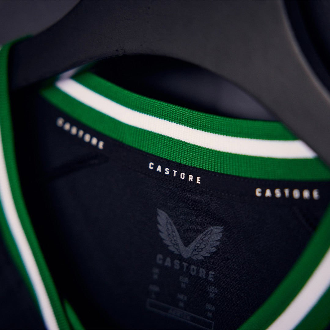MrAe9bnzmIH8Ygb | UAE SPORT STORE Close-up of a dark navy Castore jersey with green and white striped collar on a hanger.