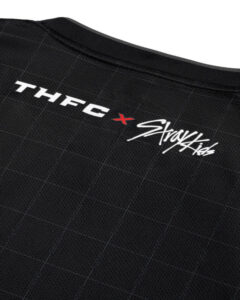 Close-up of black sports jersey fabric with 'THFC' logo and a red X beside a white script logo.