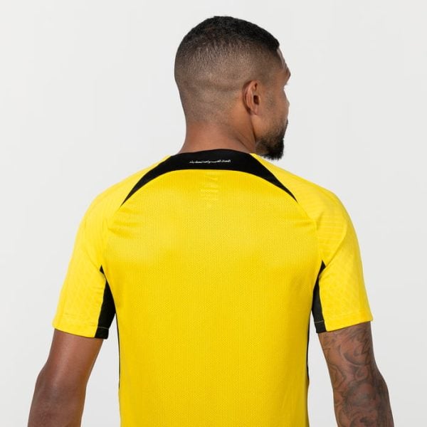 Back view of a person wearing a bright yellow athletic jersey with black accents on the shoulders and sleeves, seen from behind.