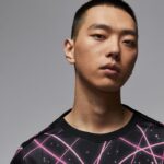 Portrait of a young Asian man with a neutral expression wearing a black shirt featuring pink geometric lines.