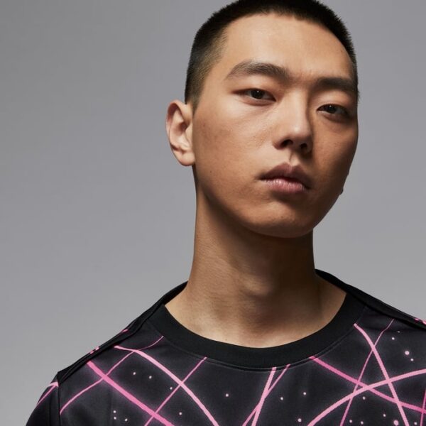Portrait of a young Asian man with a neutral expression wearing a black shirt featuring pink geometric lines.