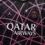 Close-up of a Paris Saint‑Germain football jersey with pink geometric lines, featuring the PSG crest and the Qatar Airways sponsor across the chest.