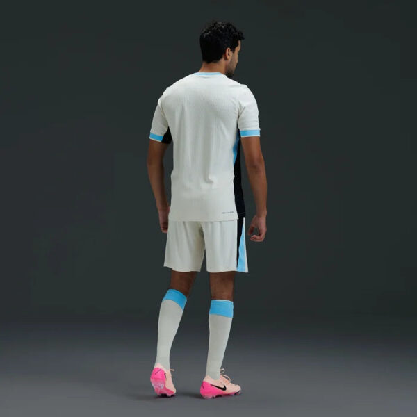 Soccer player shown from behind in a white kit with blue accents and pink cleats.