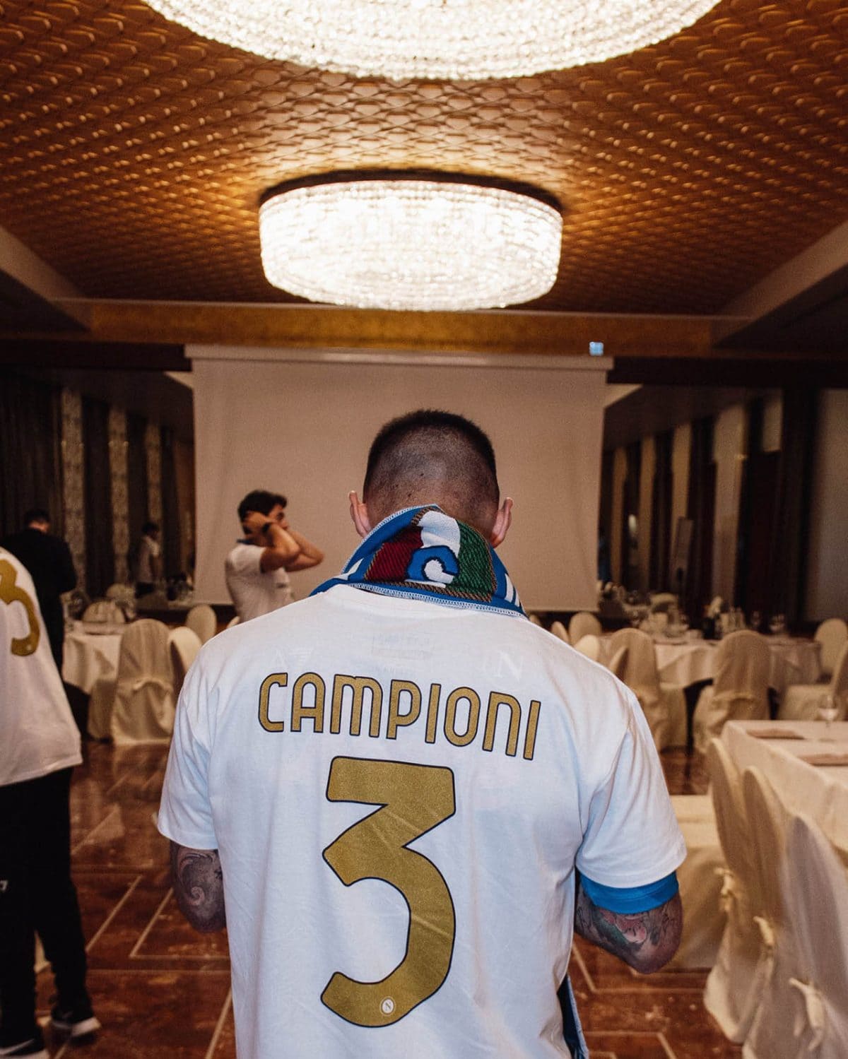 Back view of a person wearing a white jersey with 'CAMPIONI' and the number 3, in a banquet hall setting.