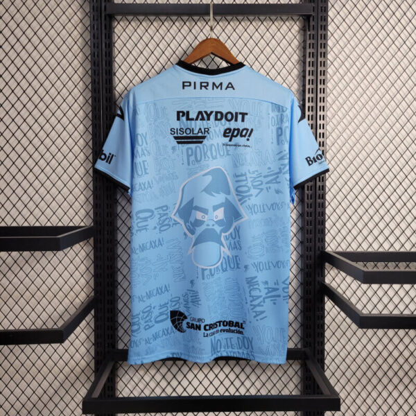 Light blue sports jersey hanging on a wooden hanger against a metal grid, showing back logos and a cartoon mascot in the center graphic.