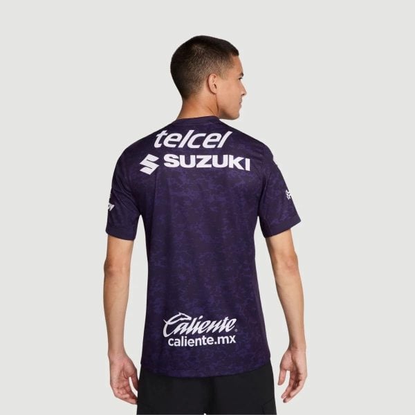 Back view of a man wearing a purple patterned sports jersey with telcel, SUZUKI, and Caliente logos.