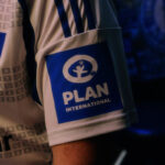 Sleeve patch with the PLAN International logo on a white sports jersey.