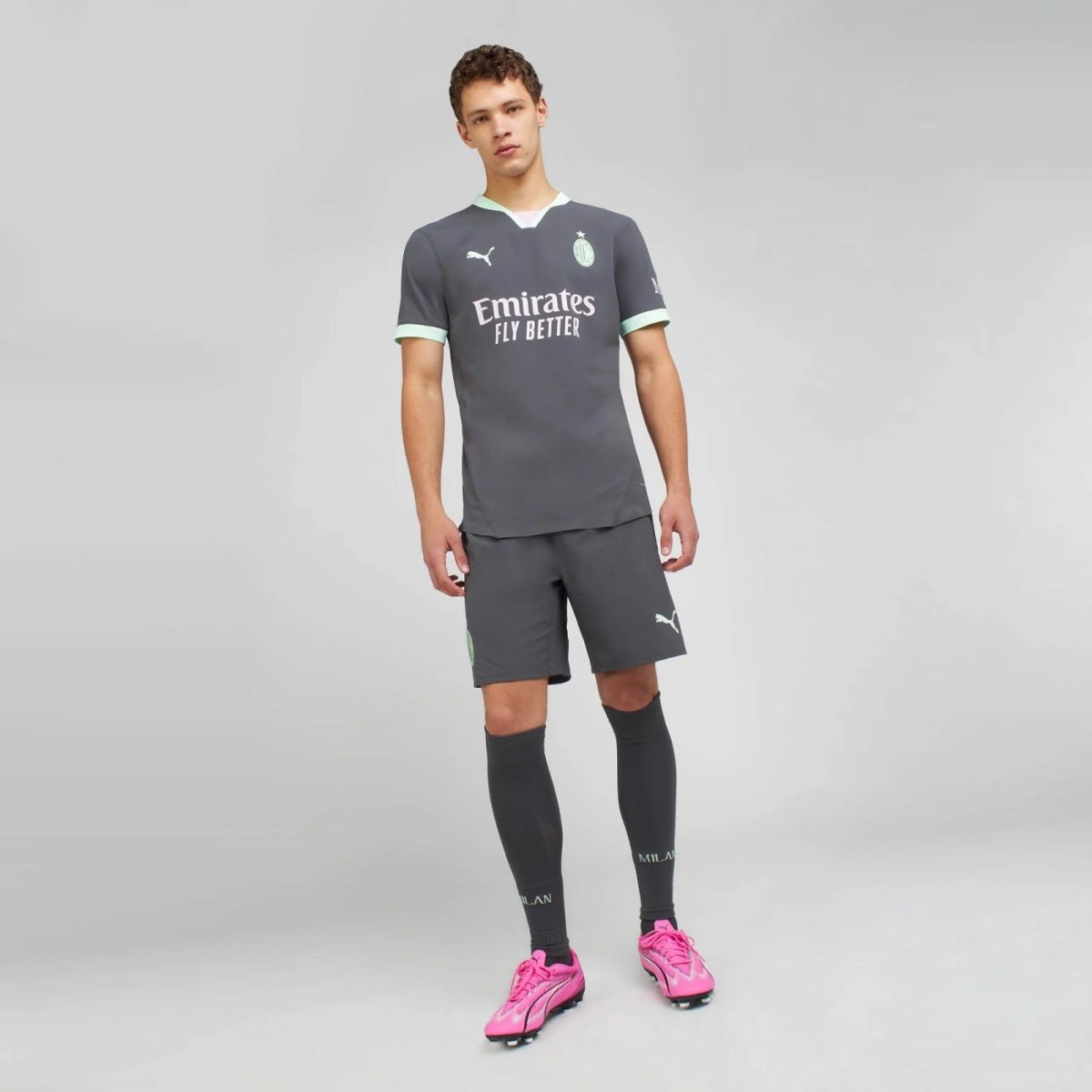Male model wearing a dark gray football kit with pale green trim and Emirates Fly Better sponsor, standing in a neutral studio background.