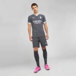 Male model wearing a dark gray football kit with pale green trim and Emirates Fly Better sponsor, standing in a neutral studio background.