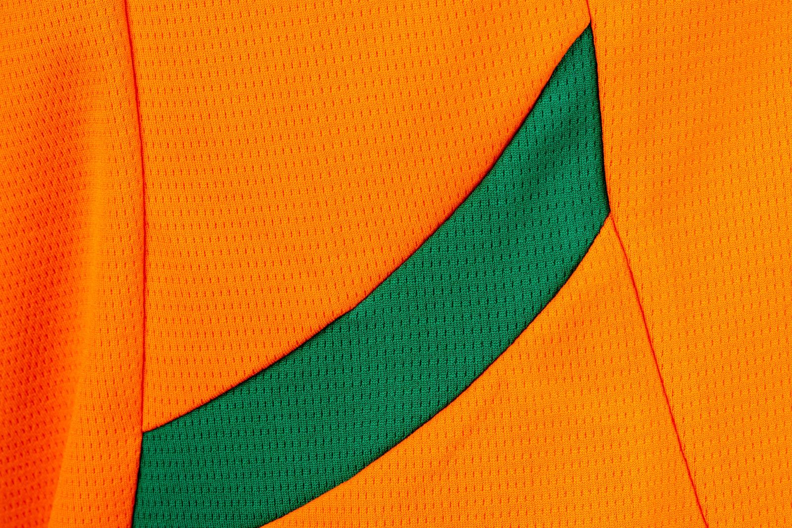 O1mNaiJU6QUxGT8 | UAE SPORT STORE Close-up of bright orange textured fabric with a dark green curved stripe across it.