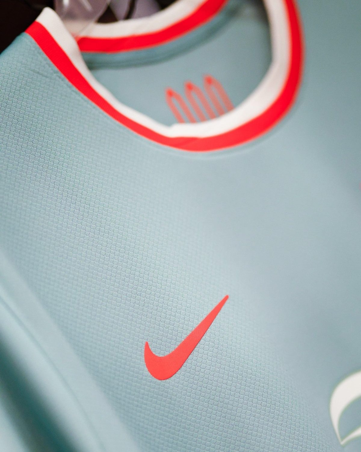 Close-up of a light blue athletic jersey showing a red Nike swoosh and red-trimmed collar.