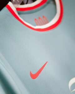 Close-up of a light blue athletic jersey showing a red Nike swoosh and red-trimmed collar.