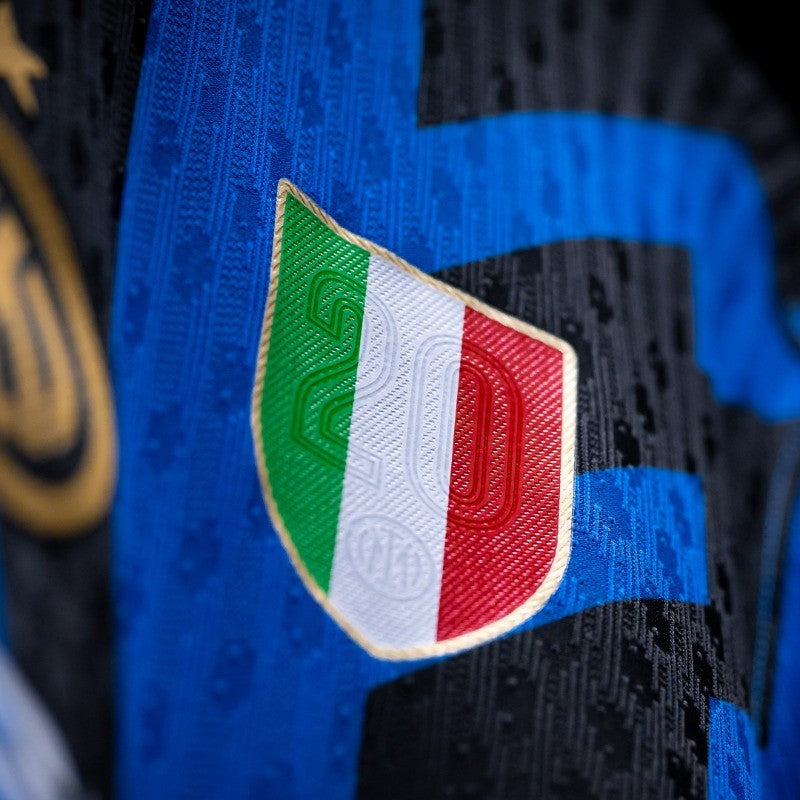 OJqX54CtojBYTYt | UAE SPORT STORE Close-up of a sports jersey with an Italian flag shield patch on blue and black striped fabric.