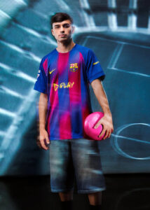 OU | UAE SPORT STORE Young man in FC Barcelona jersey holding a pink soccer ball, standing against a blurred blue backdrop.