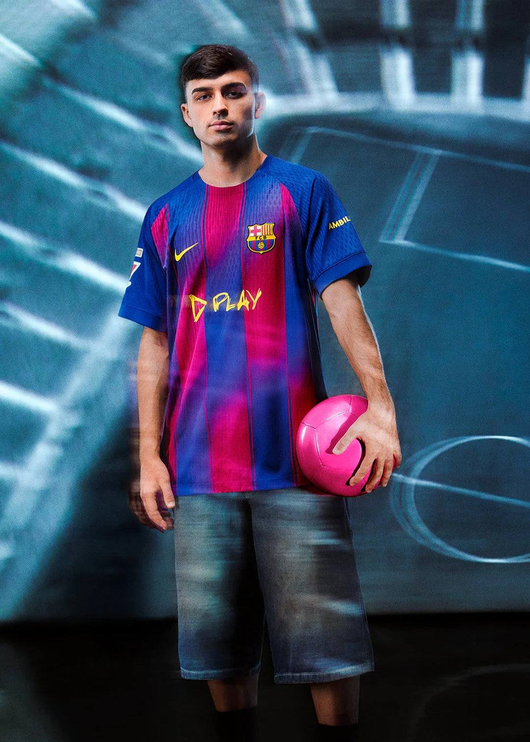 OU | UAE SPORT STORE Young man in FC Barcelona jersey holding a pink soccer ball, standing against a blurred blue backdrop.