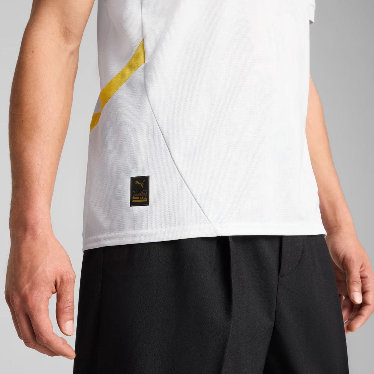 Close-up of a white jersey with a diagonal yellow stripe and a small black label reading Authentic Licensed Football near the hem.