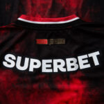 Back of a black and red sports jersey with a large white 'SUPERBET' sponsor and a small red 'TORCIDA QUE CONDUZ' above.