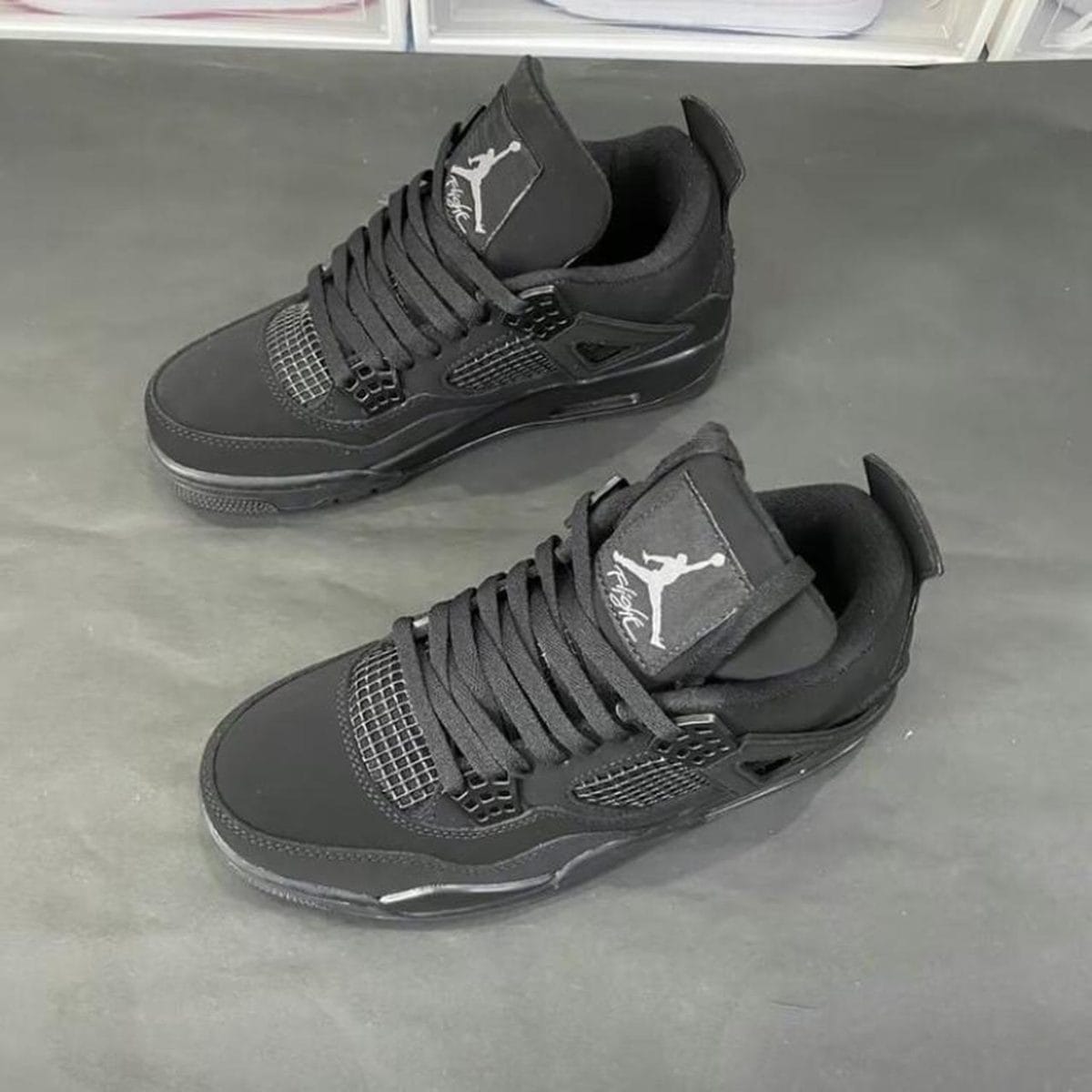Pair of black Air Jordan 4 sneakers with mesh panels and Jumpman logo on the tongue, placed on a dark surface