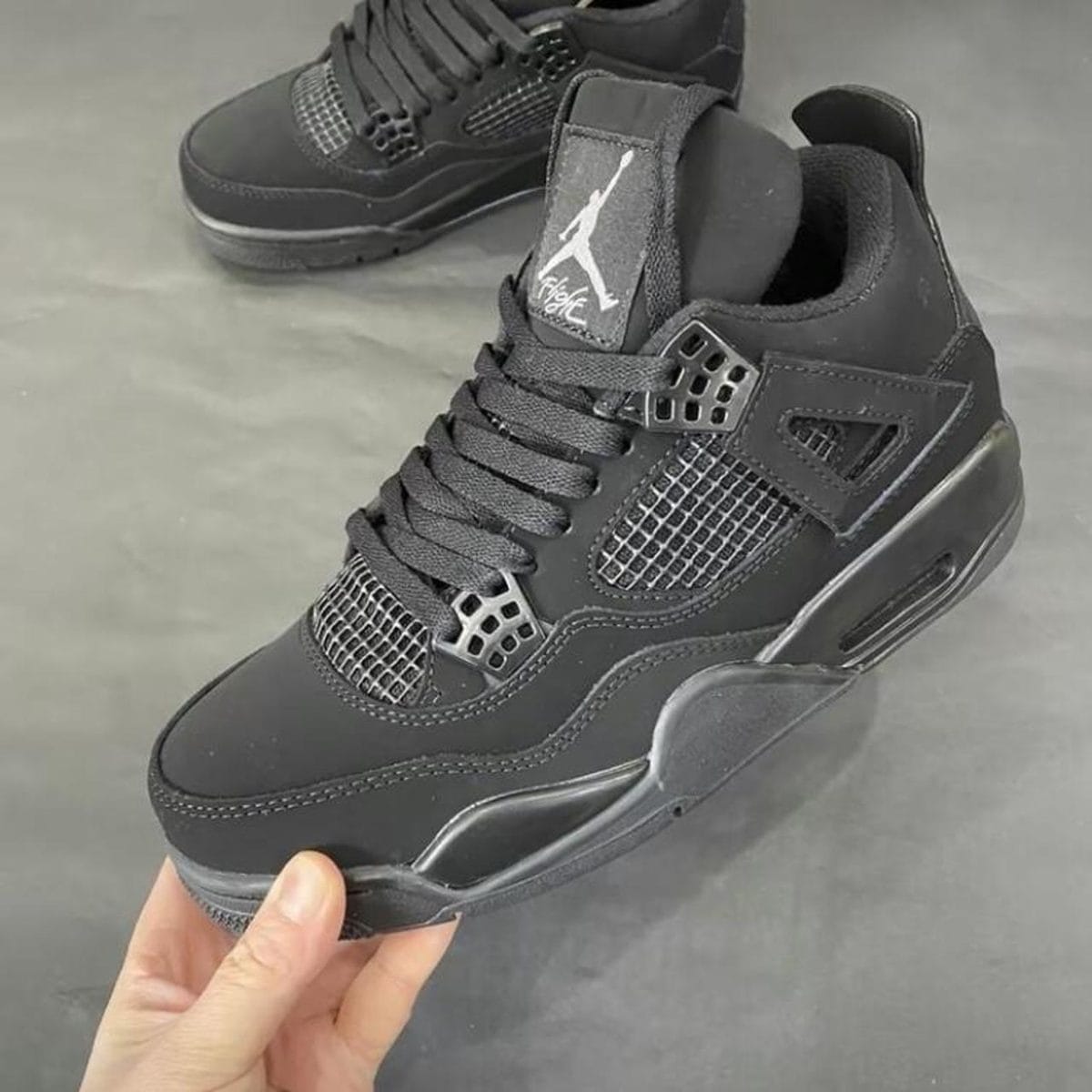 Black Air Jordan sneakers with mesh side panels and black laces on a gray surface