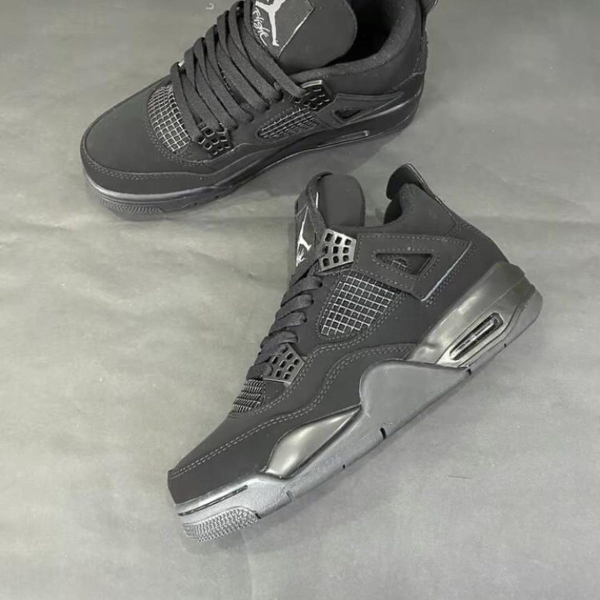 Black athletic sneakers with mesh panels resting on a gray floor, one shoe angled to show the side and sole
