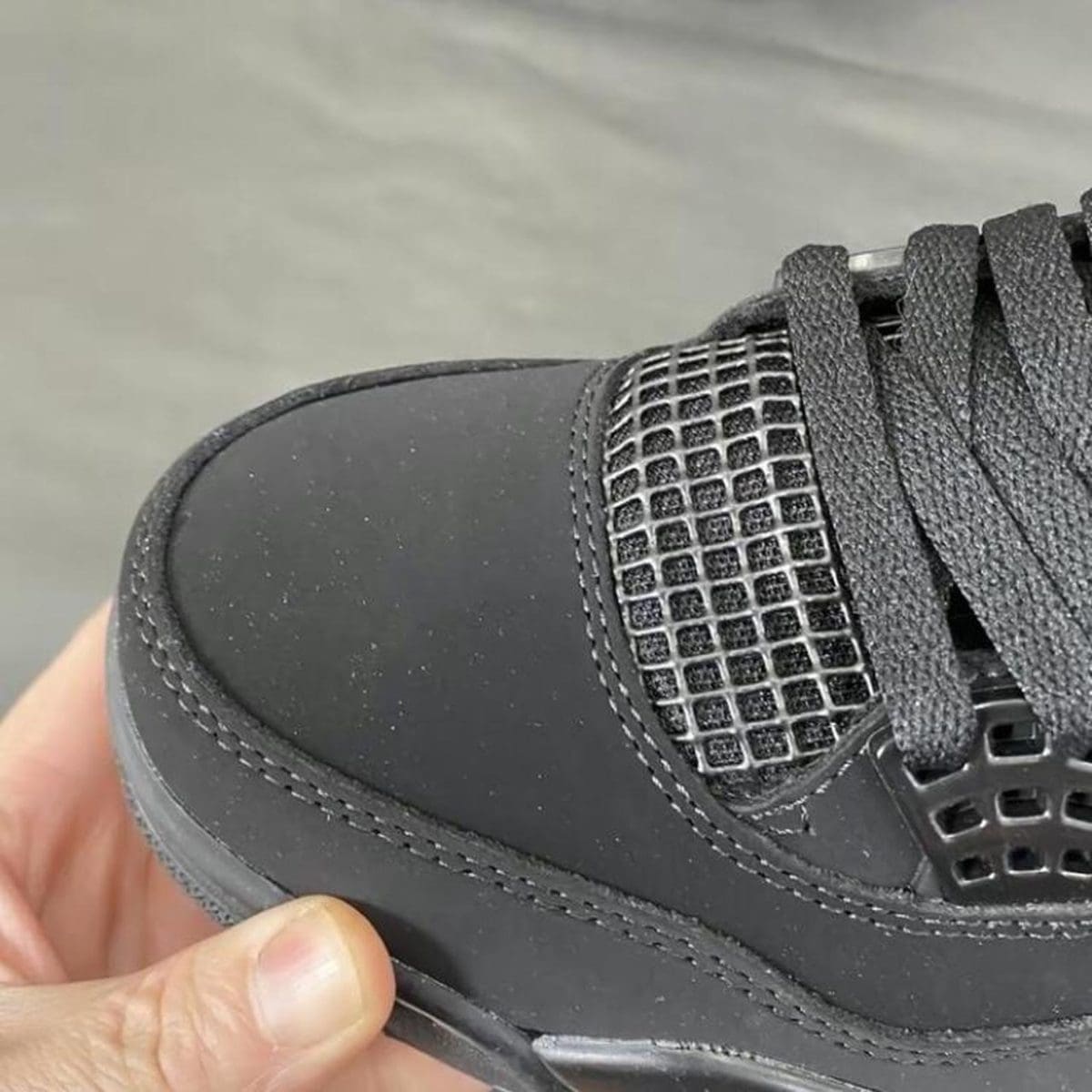 Close-up of a black sneaker toe with stitched panel and square mesh vent near the laces.