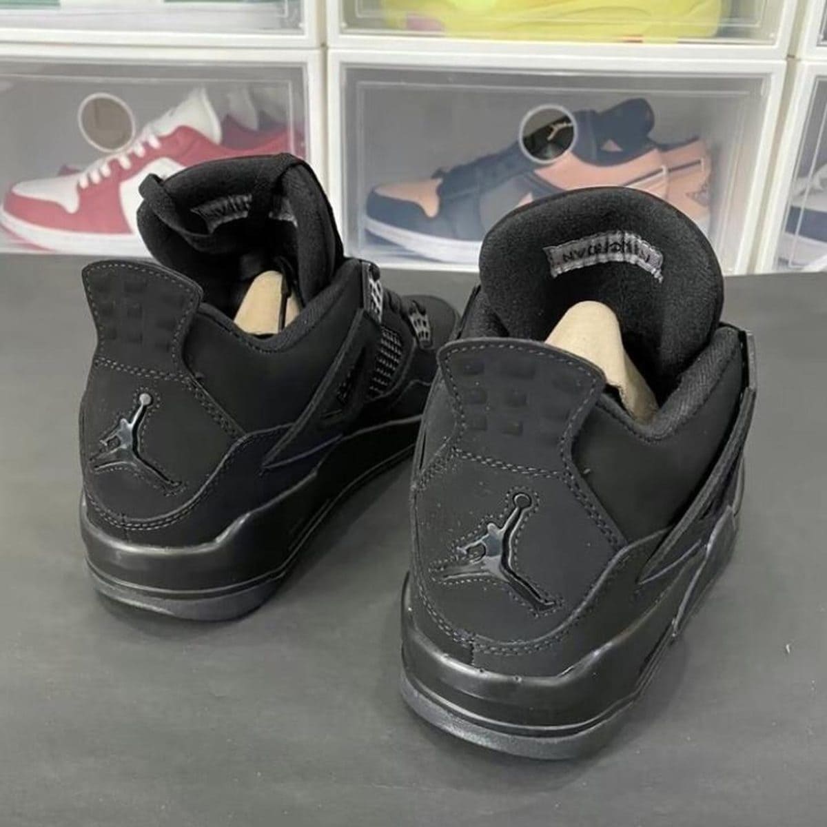 Pair of black Jordan sneakers with Jumpman logo on heel, displayed on a table with shoe storage in the background.