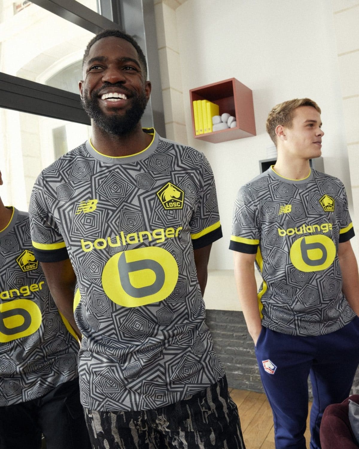 Three men in gray geometric LOSC soccer jerseys pose indoors, smiling.