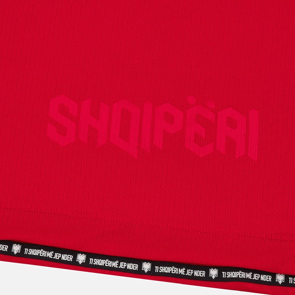 PLYECdx1jX73VPX | UAE SPORT STORE Close-up of red fabric with a faint pink wordmark and a black elastic hem with white repeating text.