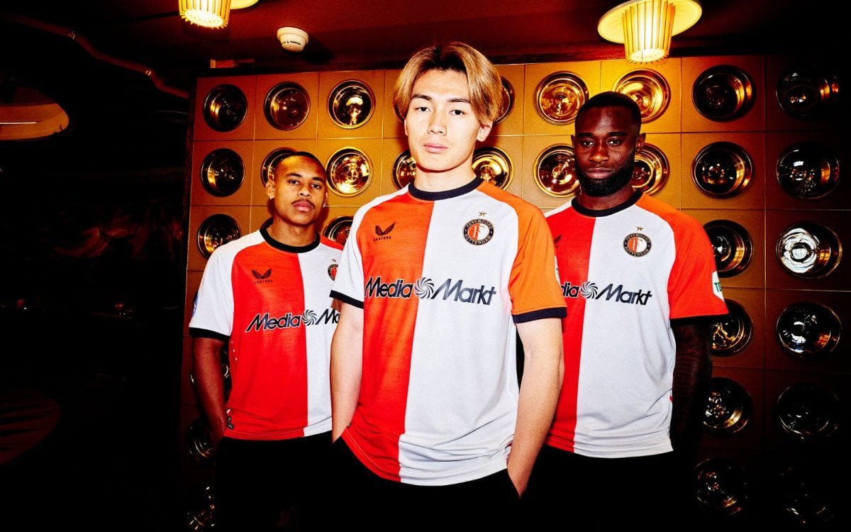 Three men in red-and-white sports jerseys pose together in a neon-lit room with a circular metallic wall behind them, signaling team unity.