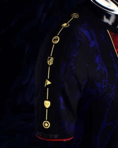 Close-up of a dark jacket sleeve with vertical gold embroidered symbols along the seam, set against a blue patterned fabric and dark background.