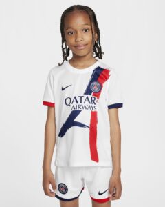 Smiling girl wearing a white Paris Saint‑Germain football jersey with red and blue brushstroke graphics and crest on the chest.