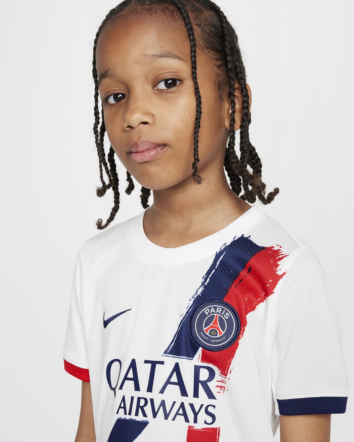 Close-up of a young girl with braids wearing a white Paris Saint‑Germain jersey featuring a blue and red splash and the Qatar Airways sponsor.